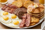 A Hearty Breakfast Spread A white plate heaped with fried eggs, sausage patties, crispy bacon, golden pancakes, and a pile of hash browns.