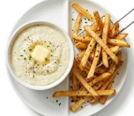 Grits-and-French-Fries-Side-Dish-Clear-Shot A divided plate featuring a bowl of buttery grits and a side of golden french fries.