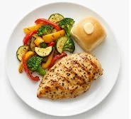Healthy-Grilled-Chicken-Breast-Dinner A grilled chicken breast with a roasted vegetable mix and dinner roll.