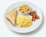 Kids-Scrambled-Egg-Breakfast-Combo Kids' breakfast plate with one scrambled egg, toast, fruit cup, and bacon.